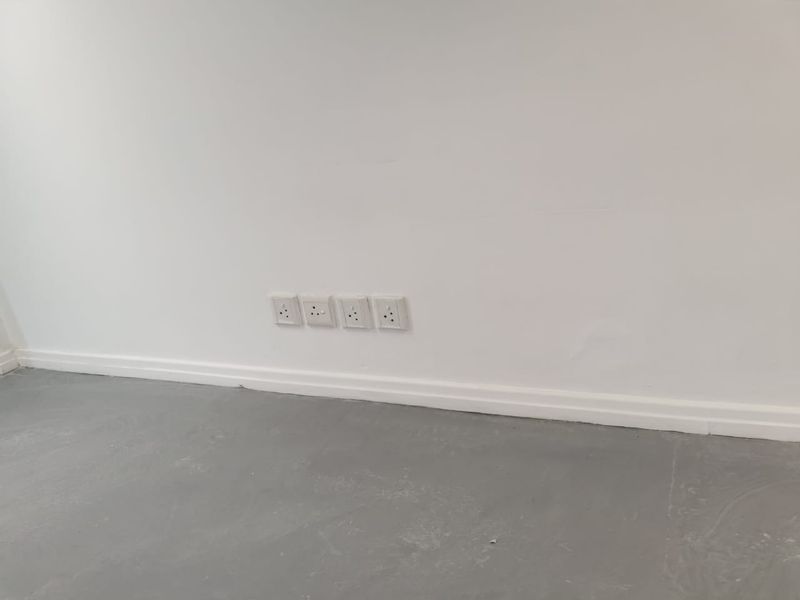 A view of a plain interior wall featuring multiple electrical power outlets and white skirting boards above a grey floor surface.