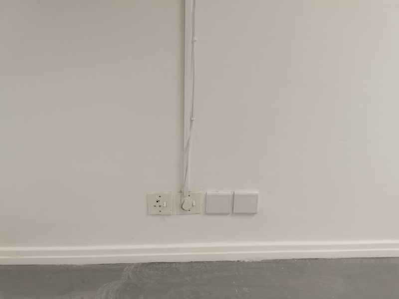 A close-up view of a wall featuring surface-mounted electrical conduit and multiple power outlets above a concrete floor.