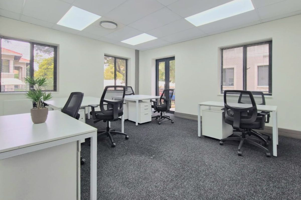 A bright, modern commercial office space featuring recessed ceiling lighting, dark carpeting, and multiple windows providing natural light.