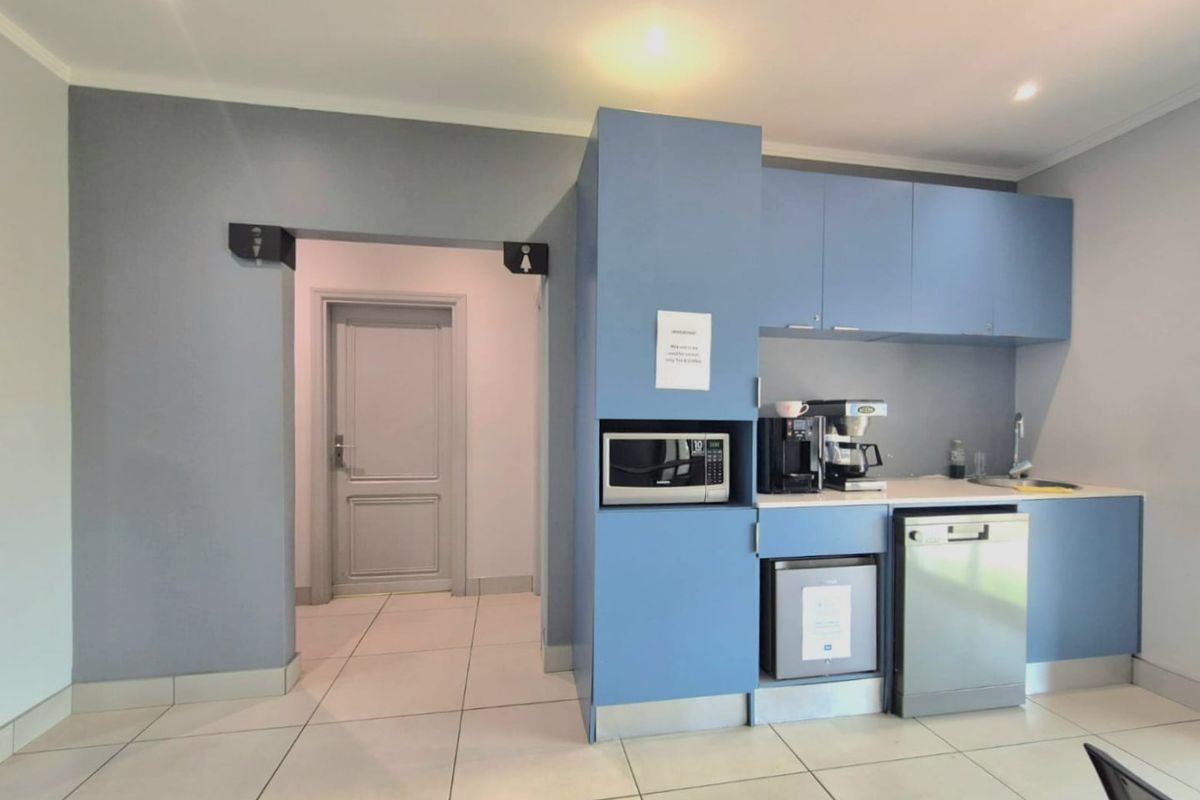 A compact kitchenette area featuring blue cabinetry, a built-in microwave, a sink, and a dishwasher, adjacent to a doorway leading to restroom facilities.