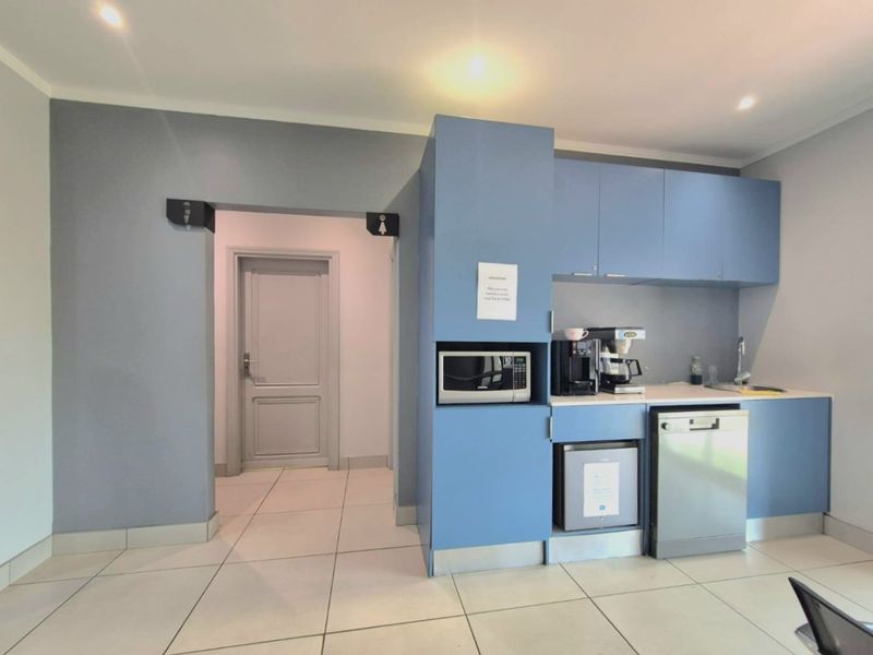 A compact kitchenette area featuring blue cabinetry, a built-in microwave, a sink, and a dishwasher, adjacent to a doorway leading to restroom facilities.