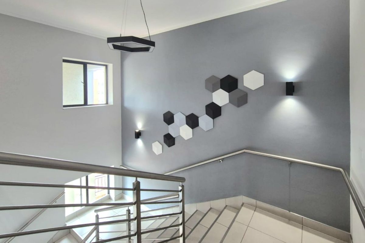 A modern stairwell featuring tiled flooring, stainless steel handrails, and decorative geometric wall panels with integrated wall lighting.