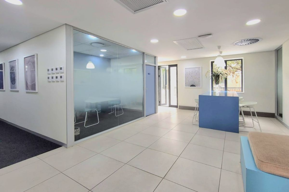 Modern commercial office space featuring tiled flooring, recessed ceiling lighting, central air conditioning, and a glass-partitioned meeting room.