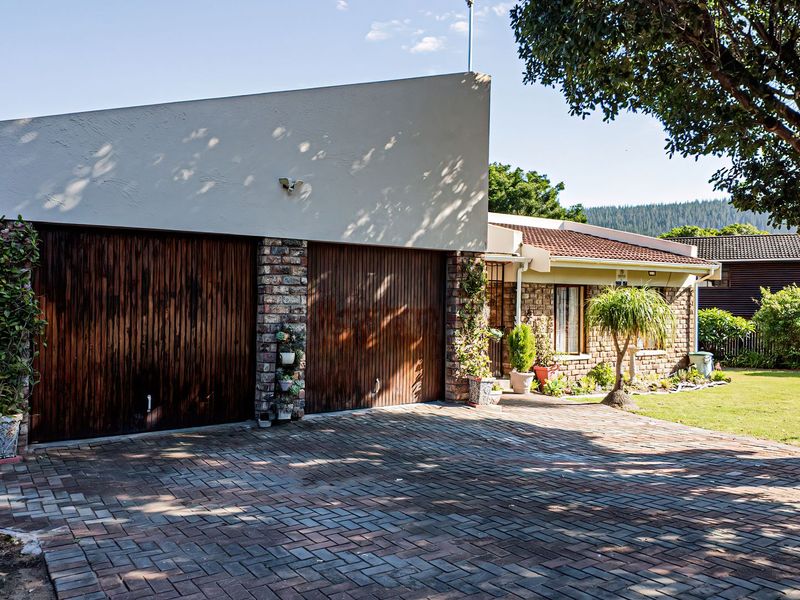 Front view of a residential property featuring a double garage with timber doors, a brick-paved driveway, and established garden surroundings.