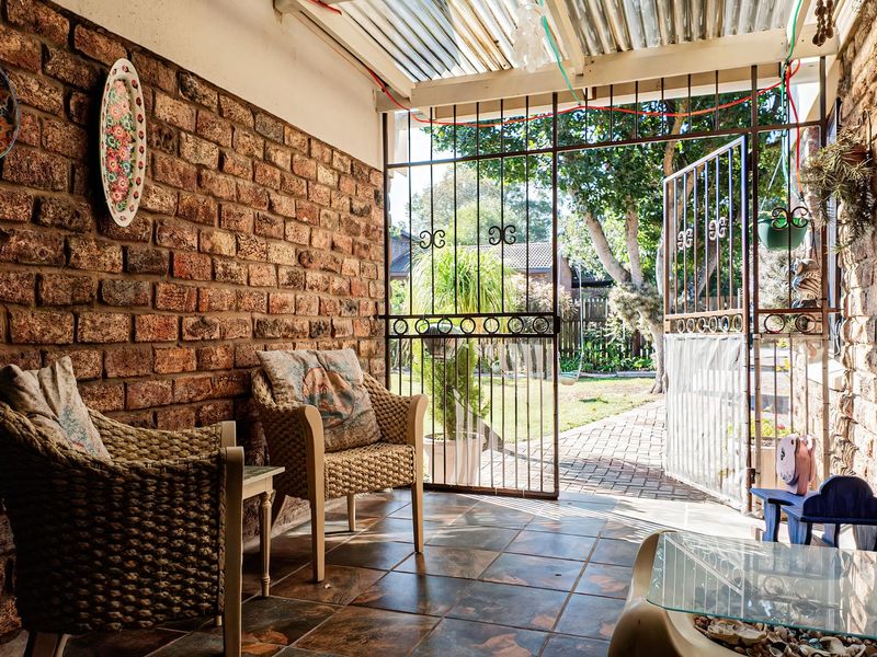 A covered patio area featuring exposed brick walls, tiled flooring, and a secure wrought iron gate leading to the garden.