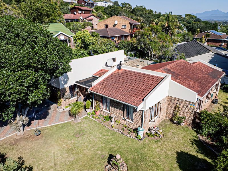 Aerial view of a residential property featuring a brick facade, tiled roof, paved driveway, and a well-maintained garden area.