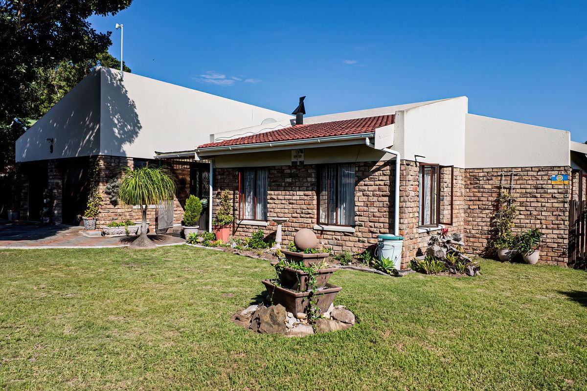 A rear view of a face brick house featuring a tiled roof, chimney, and a well-maintained garden with a paved patio area.