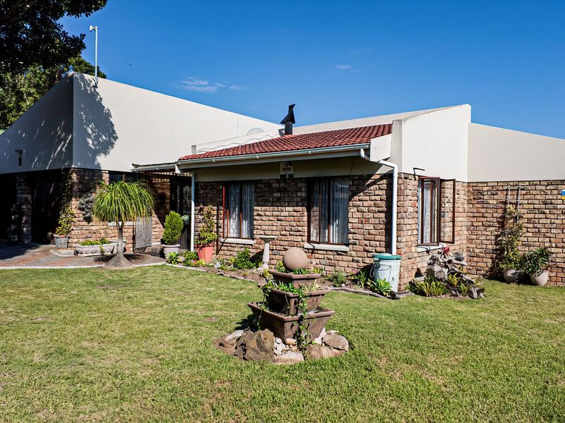 A rear view of a face brick house featuring a tiled roof, chimney, and a well-maintained garden with a paved patio area.