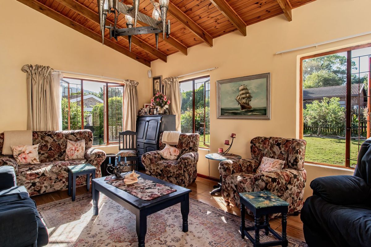 A cozy living room featuring a high exposed timber beam ceiling, tiled flooring, and large windows providing ample natural light and garden views.