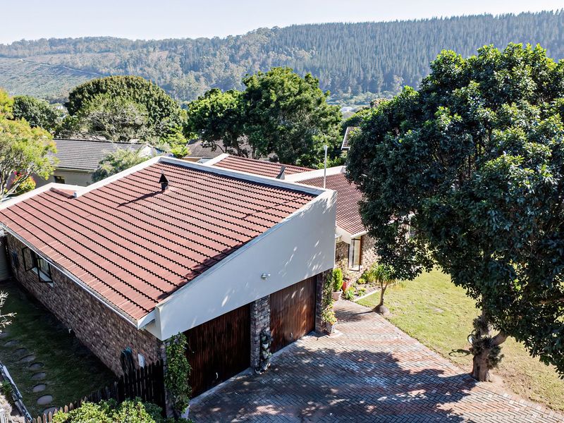 Aerial view of the property featuring a tiled roof, double garage, brick exterior, and a paved driveway set within a landscaped garden.