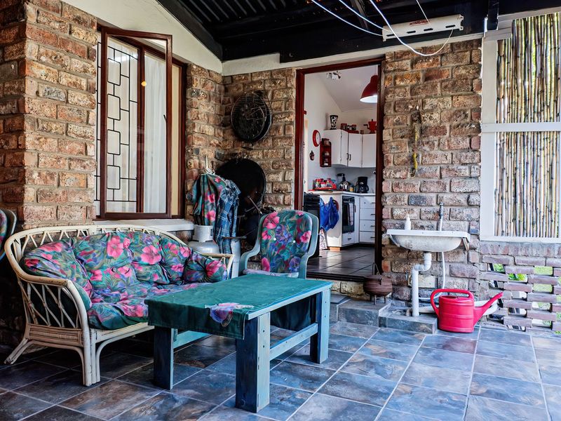A covered patio area featuring exposed brick walls, slate tile flooring, and a built-in utility sink, providing direct access to the kitchen interior.