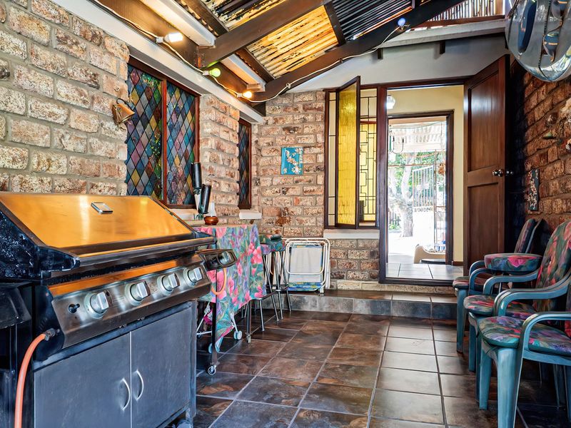 Covered patio area featuring exposed brick walls, stained glass windows, tiled flooring, and a built-in braai, offering a rustic outdoor entertainment space.
