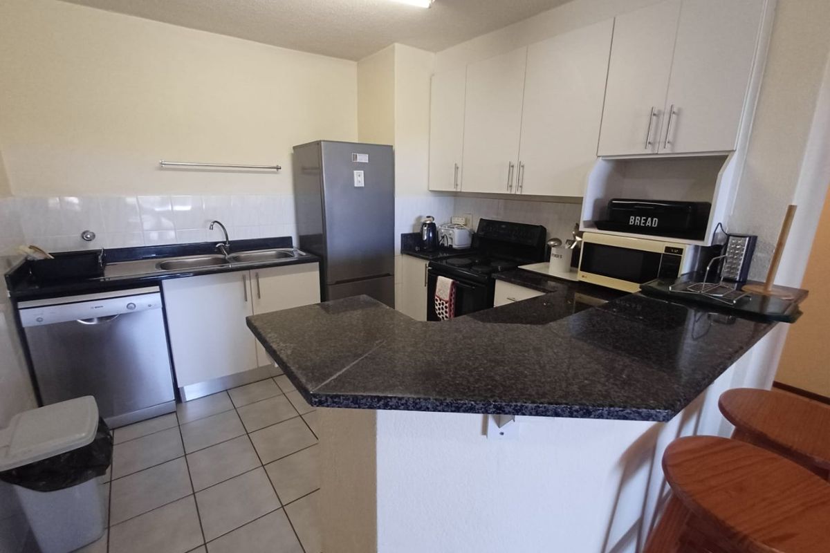 A functional kitchen featuring white cabinetry, dark granite countertops, a breakfast bar, and tiled flooring, providing a practical layout for daily use.