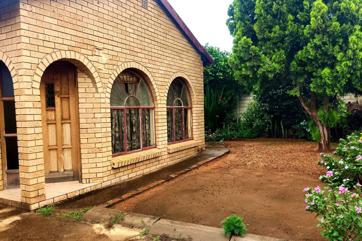 A rear view of a face brick house featuring arched windows with security bars, a wooden entrance door, and a garden area.