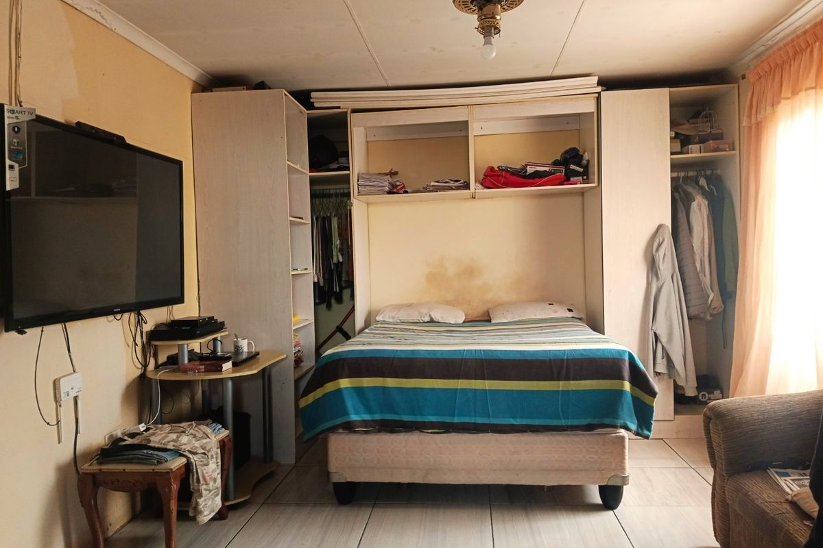 Bedroom featuring built-in cupboards, tiled flooring, and a ceiling fan. The room shows signs of wear, including water staining on the wall.