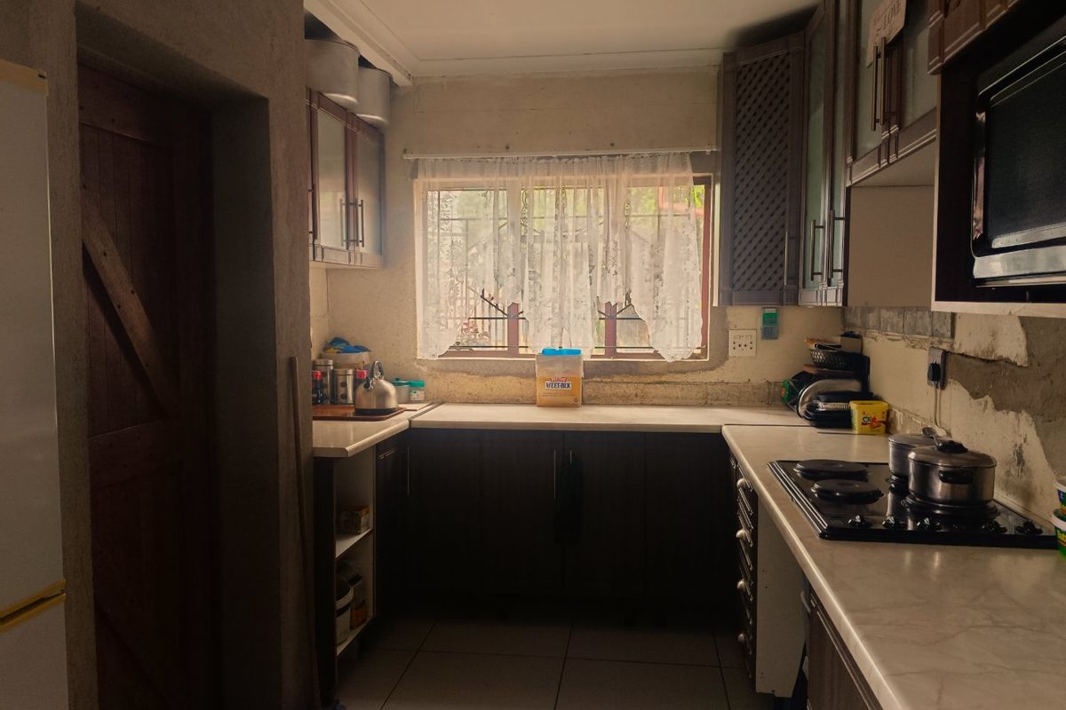 A functional kitchen featuring dark cabinetry, laminate countertops, and a built-in hob, with unfinished wall surfaces requiring cosmetic attention.