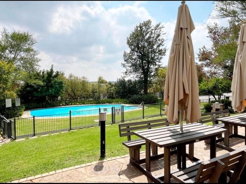 A well-maintained communal pool area featuring a paved patio, landscaped lawn, and secure metal fencing, ideal for outdoor relaxation and recreation.