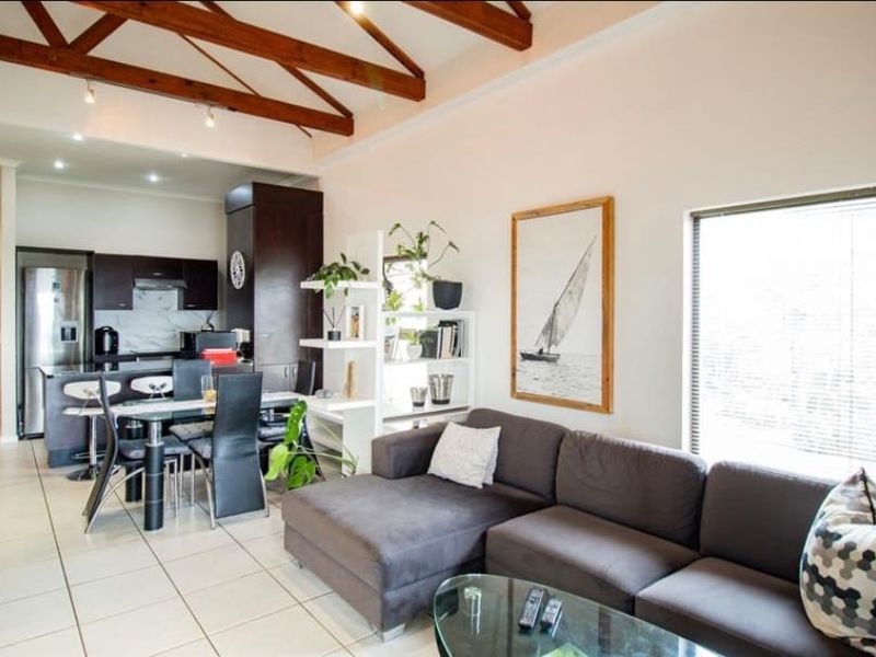 Open-plan living and kitchen area featuring exposed timber ceiling beams, tiled flooring, and modern dark cabinetry with integrated kitchen appliances.