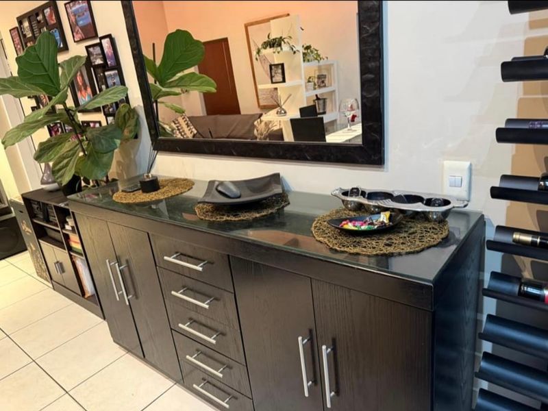 A living area featuring dark wood built-in cabinetry with a glass top, tiled flooring, and a wall-mounted wine rack.