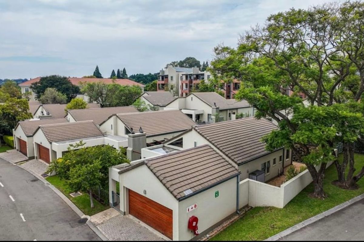 Aerial view of a residential apartment complex featuring tiled roofs, garages, and landscaped surroundings within a secure estate.