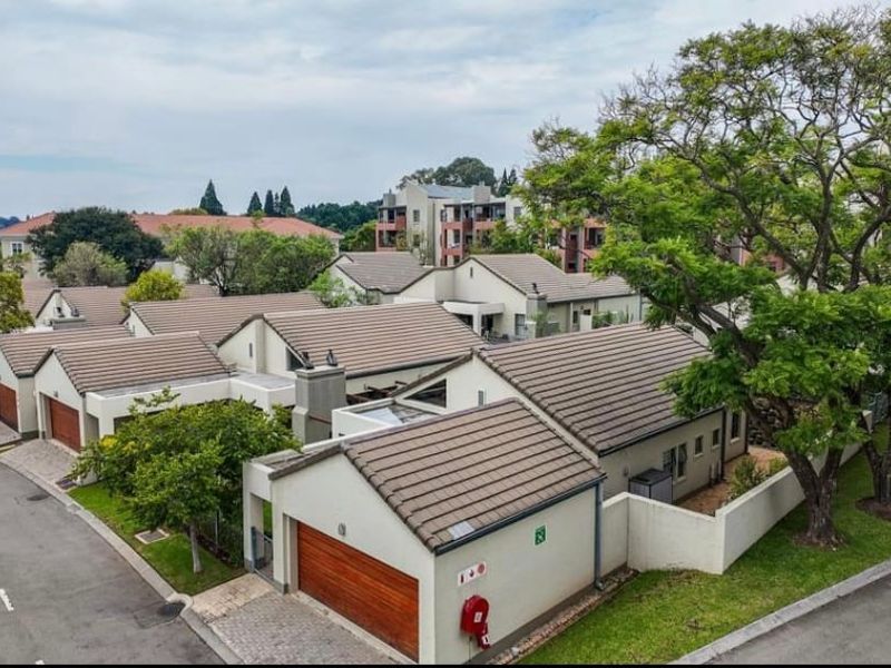 Aerial view of a residential apartment complex featuring tiled roofs, garages, and landscaped surroundings within a secure estate.