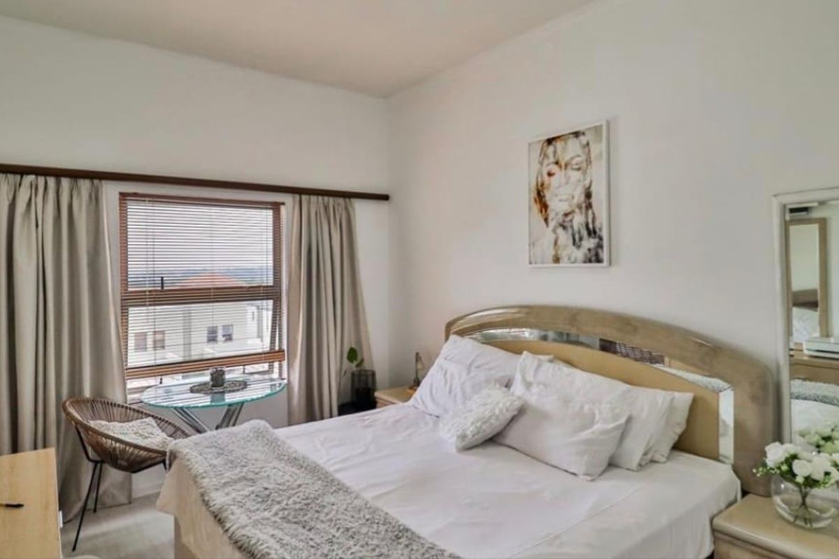 A well-lit bedroom featuring a large window with blinds and curtains, providing natural light and a view of the surrounding area.