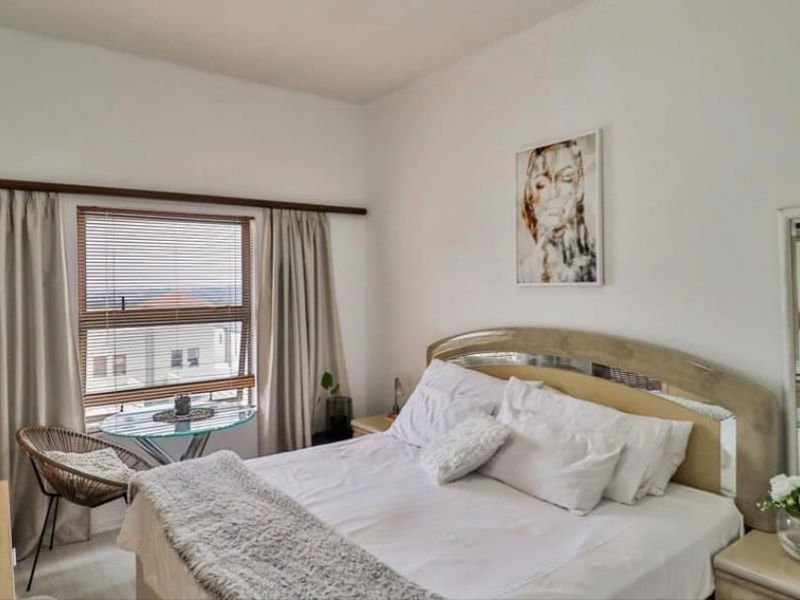 A well-lit bedroom featuring a large window with blinds and curtains, providing natural light and a view of the surrounding area.