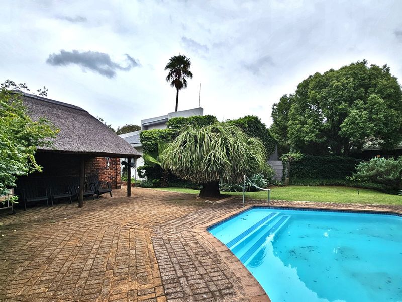 Outdoor entertainment area featuring a swimming pool with integrated steps and a covered thatched lapa set within a landscaped garden.