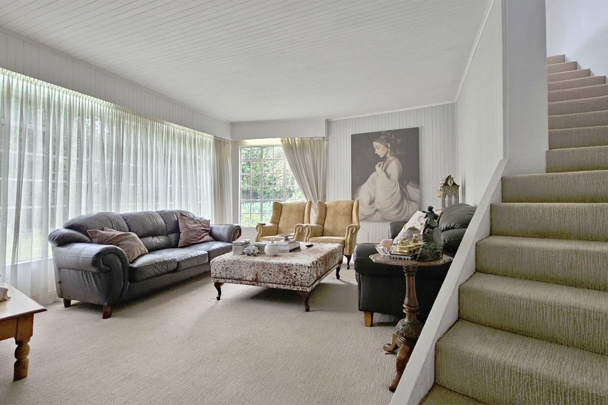 Spacious living room featuring timber panelled walls and ceiling, carpeted flooring, and an integrated staircase leading to the upper level.