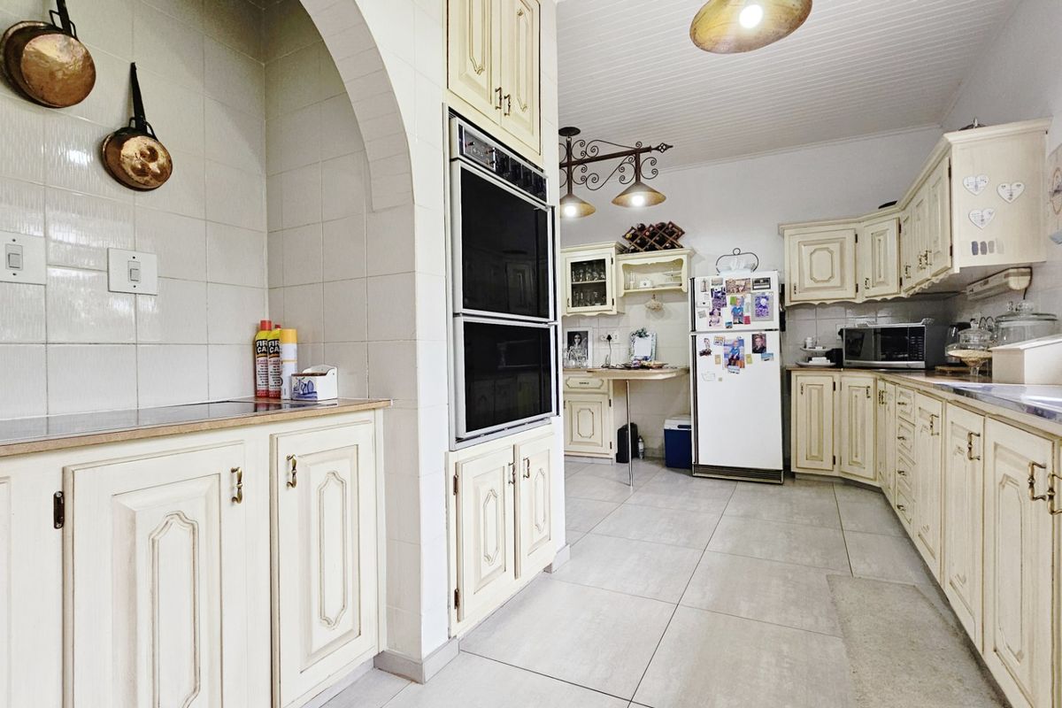 A spacious kitchen featuring traditional cream cabinetry, a built-in double oven, tiled splashbacks, and large floor tiles with a distinct architectural archway.