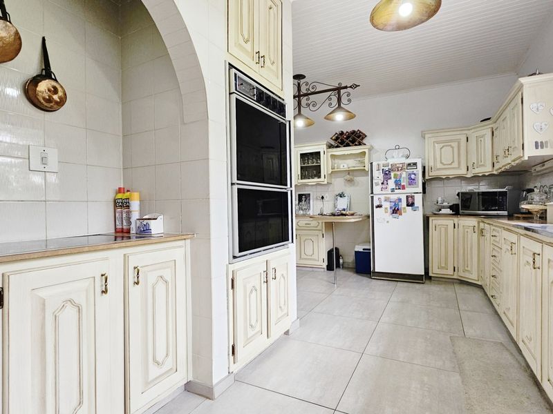 A spacious kitchen featuring traditional cream cabinetry, a built-in double oven, tiled splashbacks, and large floor tiles with a distinct architectural archway.