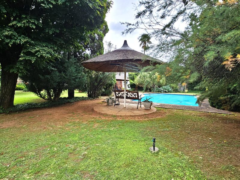 A spacious garden area featuring a swimming pool, a thatched gazebo, and mature trees, offering a private outdoor retreat.