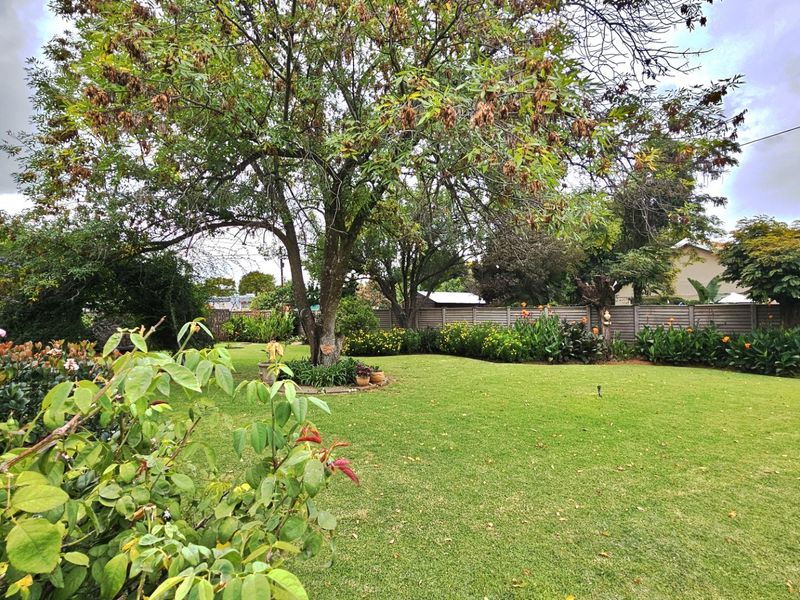 A well-maintained private garden featuring a lush green lawn, mature trees, and established perimeter fencing.