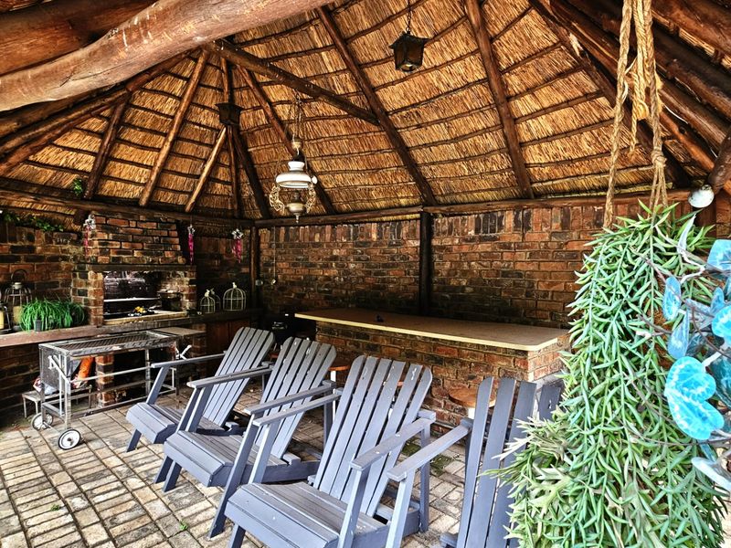 Covered outdoor entertainment area featuring a rustic thatched roof, exposed timber beams, brick walls, a built-in brick braai, and a fixed bar counter.