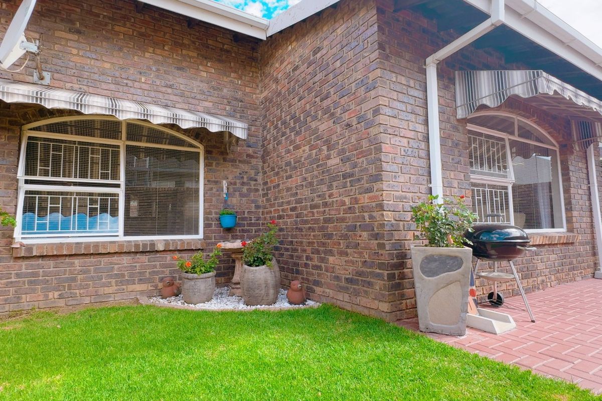 A well-maintained rear exterior view featuring a face brick facade, paved patio area, and protective window awnings.