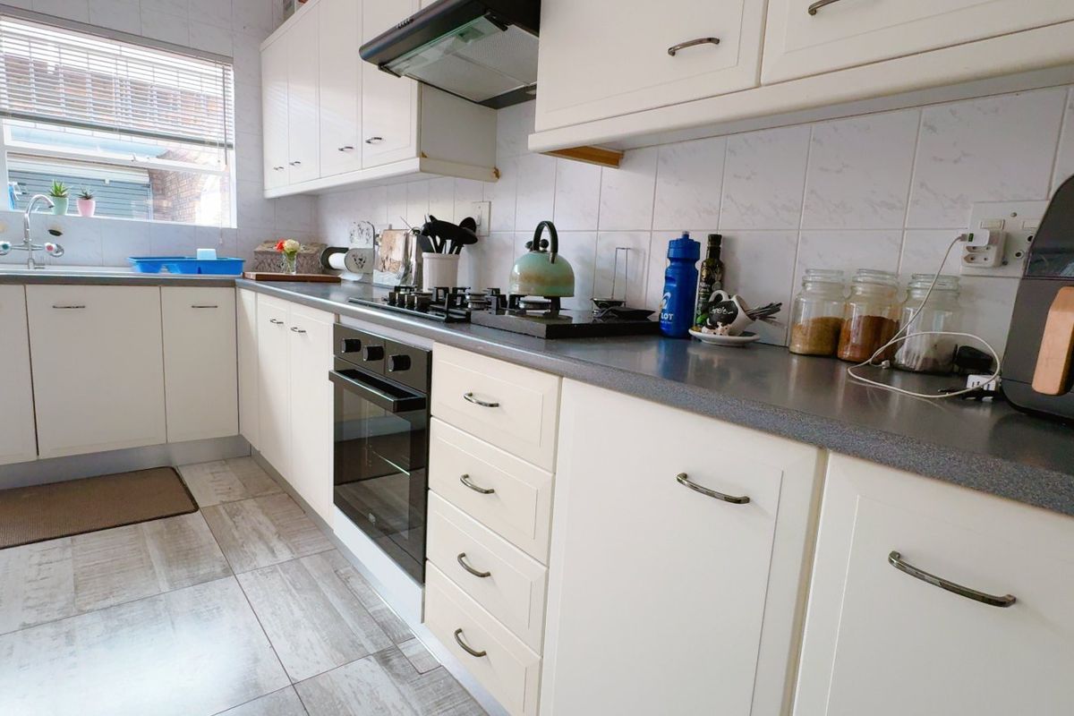 A functional kitchen featuring white cabinetry, dark laminate countertops, a built-in oven with gas hob, and tiled flooring.