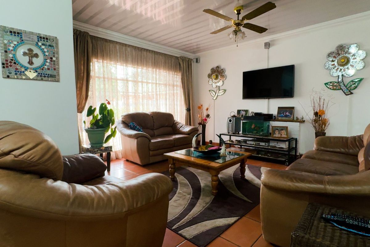 A comfortable living room featuring tiled flooring, a ceiling fan, and large windows that allow for natural light.