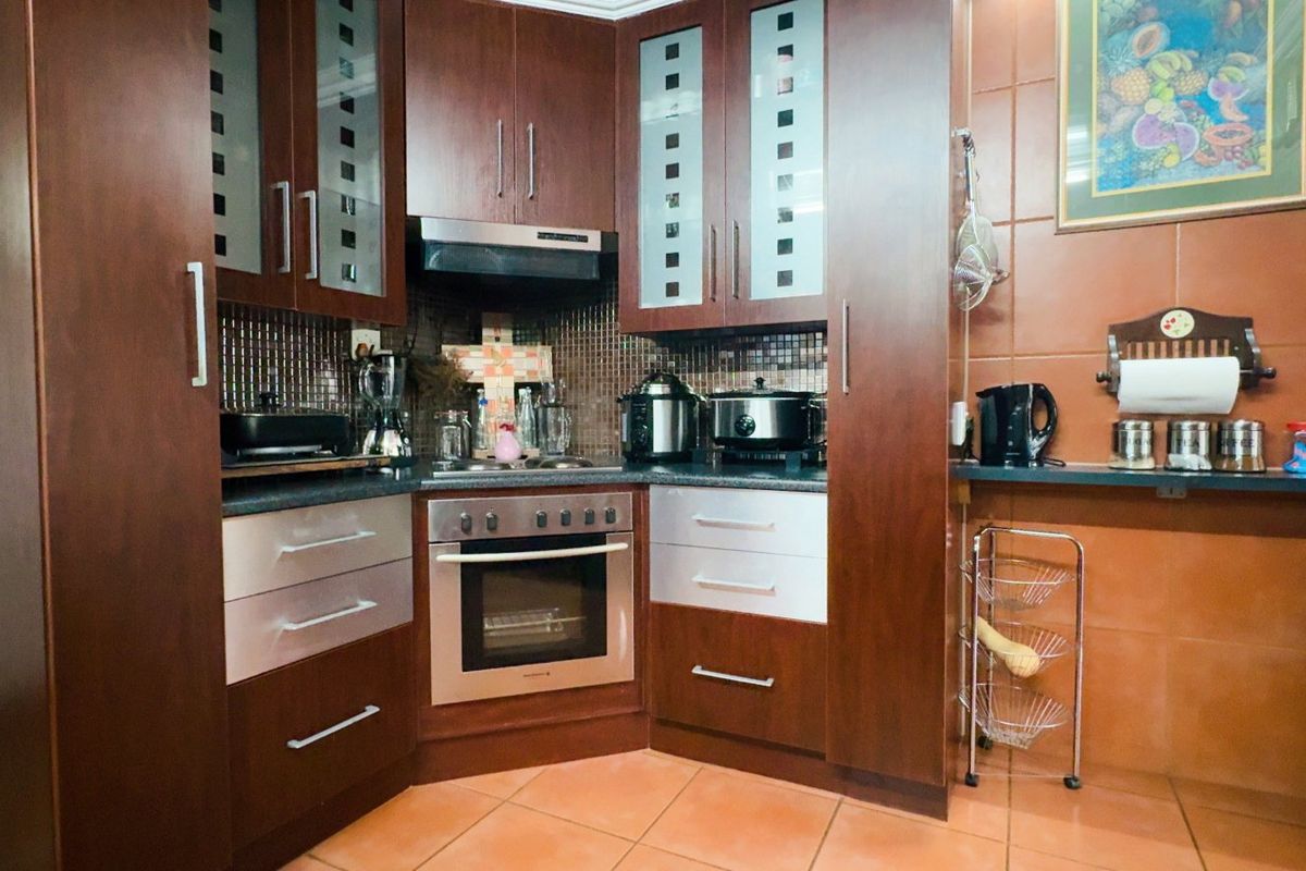 A functional kitchen featuring dark wood cabinetry, integrated oven, extractor fan, and tiled splashbacks with durable floor tiles.