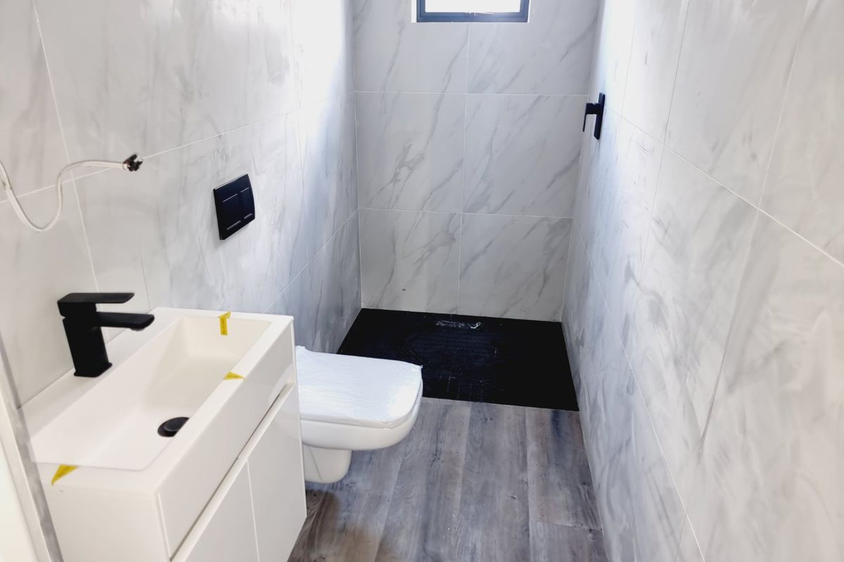 Modern bathroom featuring marble-look wall tiles, a sleek vanity with a black faucet, a wall-mounted toilet, and a dark tiled shower area.