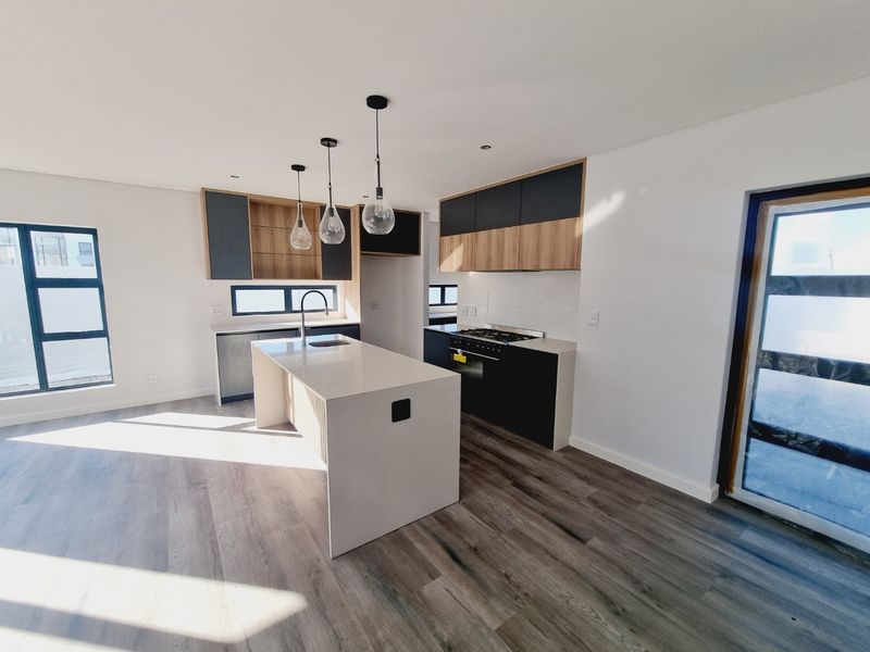 Modern open-plan kitchen featuring a central island, stone countertops, built-in gas hob, and contemporary two-tone cabinetry with wood accents.