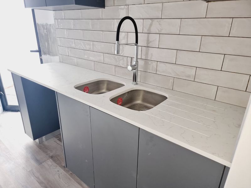 Modern kitchen featuring grey cabinetry, white marble-look countertops, a double stainless steel sink with a contemporary faucet, and white subway tile backsplash.