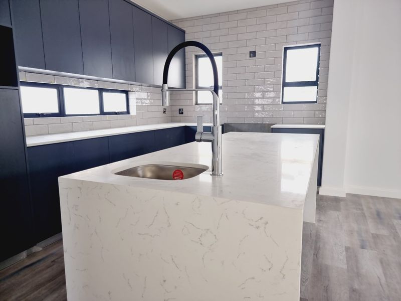 Modern kitchen featuring a large marble-look island with a prep sink, dark cabinetry, and subway tile backsplash.