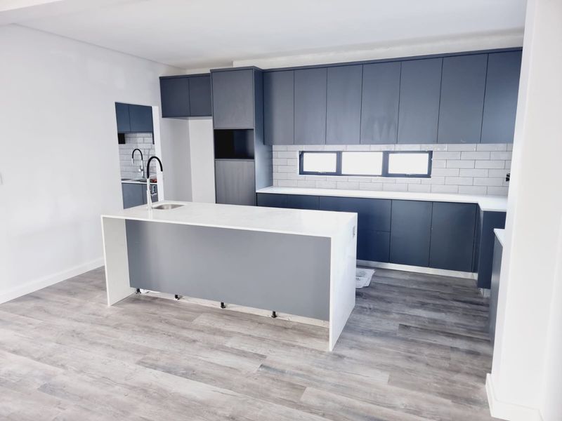 Modern kitchen featuring dark cabinetry, a central island with a stone countertop, integrated sink, and subway tile backsplash.