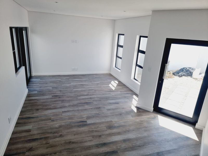 A bright, empty living room featuring modern wood-look laminate flooring, recessed ceiling lighting, and large black-framed windows and doors leading to the exterior.