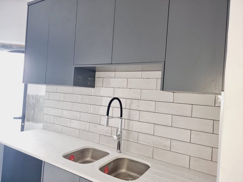 Modern kitchen area featuring sleek grey cabinetry, white subway tile backsplash, stone countertop, and a contemporary dual-basin sink with a gooseneck faucet.