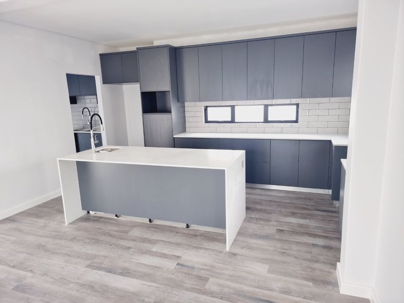 Modern kitchen featuring dark grey cabinetry, white stone countertops, a central island with a sink, and light wood-look flooring.