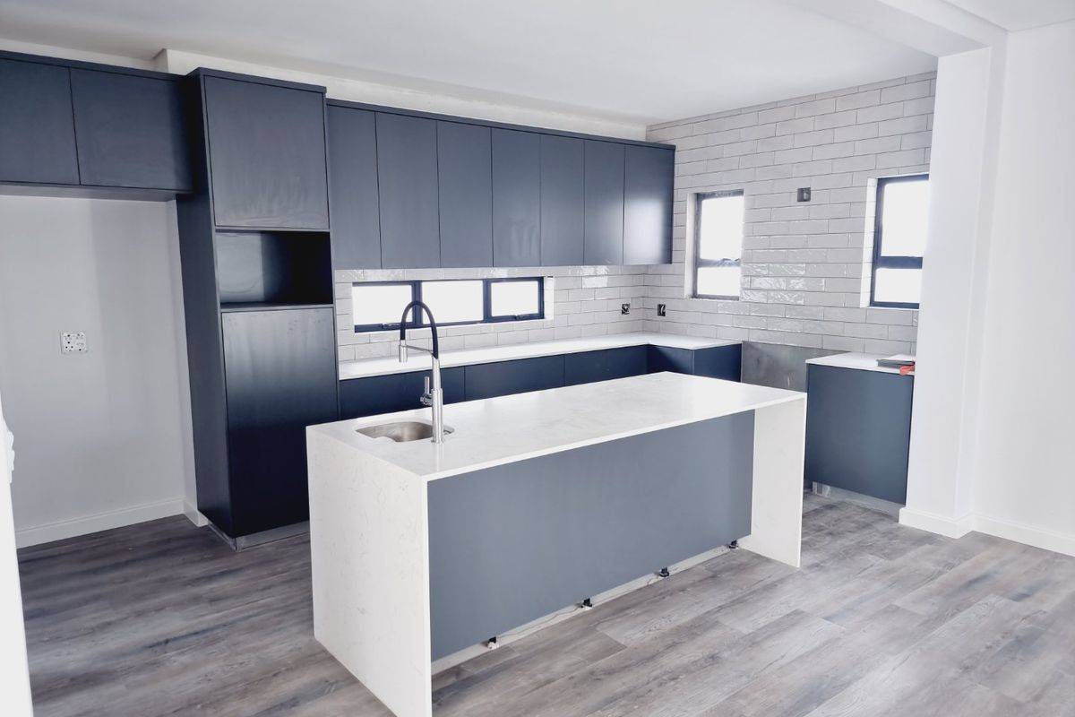 Modern kitchen featuring dark cabinetry, a central island with a stone countertop, integrated sink, and subway tile backsplash.