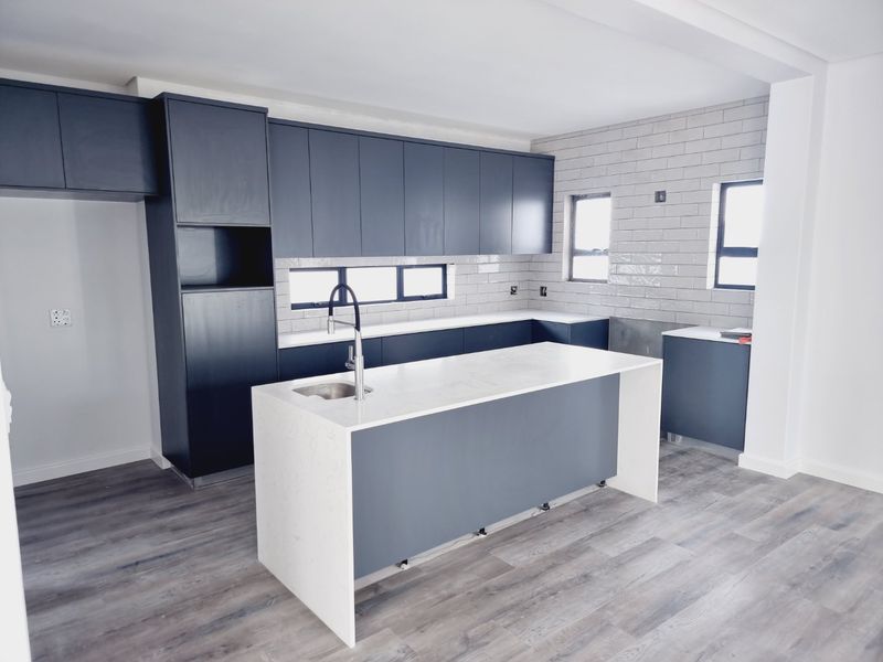 Modern kitchen featuring dark cabinetry, a central island with a stone countertop, integrated sink, and subway tile backsplash.