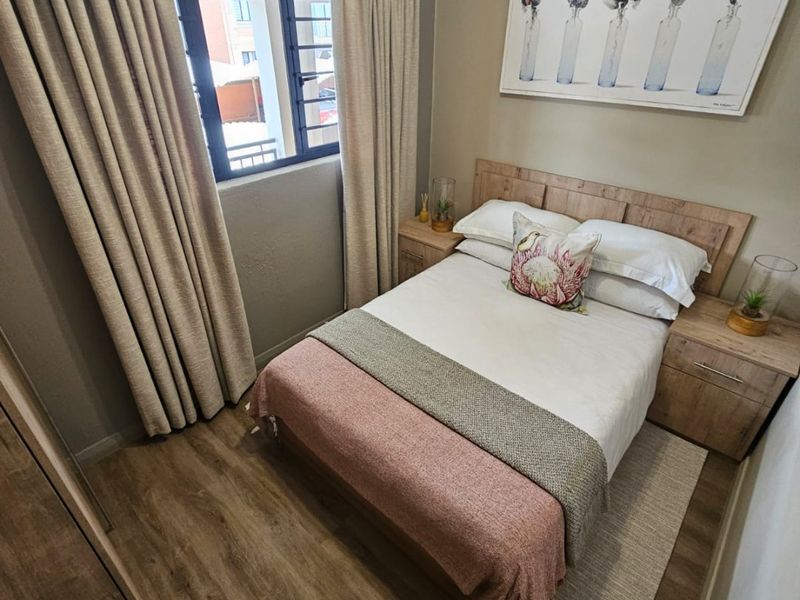 A well-maintained bedroom featuring laminate flooring, a built-in cupboard, and a window with security bars, offering a cozy and functional living space.