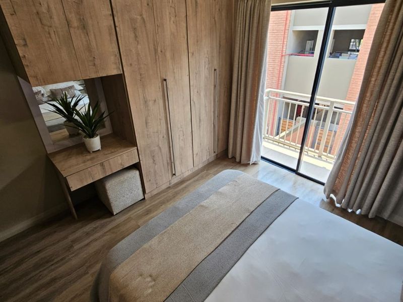 A well-maintained bedroom featuring modern wood-look built-in cabinetry with an integrated vanity and sliding glass doors leading to a private balcony.